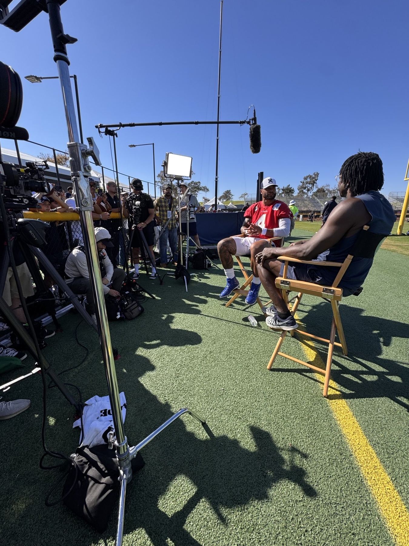 Sit-down interview on a football practice field surrounded by cameras
